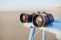 Binoculars reflecting a sunset and laying on table by the sea